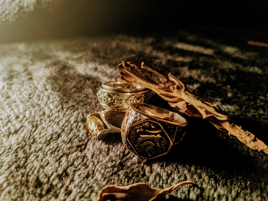 Three rings laying on a black cloth, rings have buddhis symbols on it, leaves laying nearby. Cali8Fold