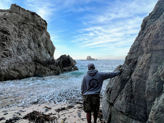 Freediver standing at the mouth of a cove, leaning against a rock, wearing a Cali8Fold hoodie,
