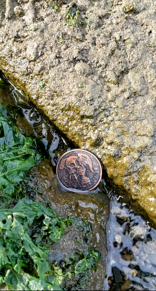 Memento Mori coin in between rocks, water flowing over, Cali8Fold