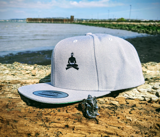 Gray hat with crossed legged diver, hat sitting on log with cove in background. Gray ring depicting Ganesh in front of hat.