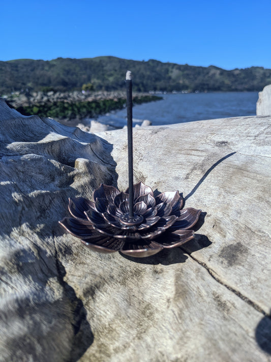 lotus shaped incense holder, sitting on log, with water in the background, incense is burning