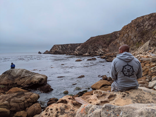 Male sitting on the shore wearing a Cali8Fold hoodie