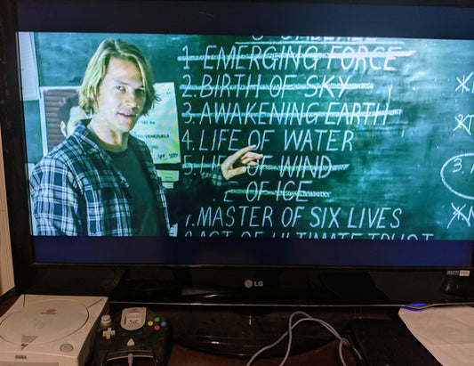 Still screen from Point Break, young white male in front of chalk board, pointing to "Life of Water" written on chalk board next to him
