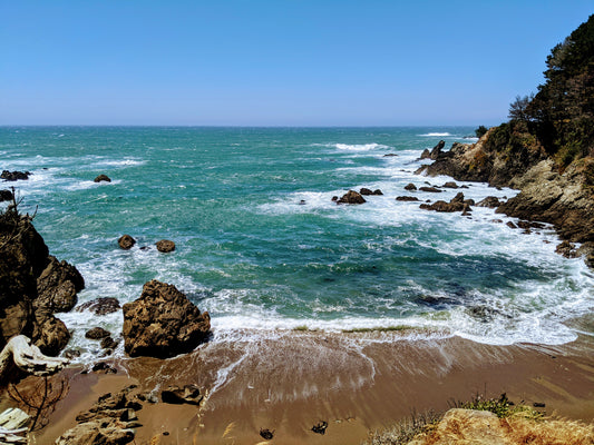 Waves crashing against brown rocks, in a cove, blue sky without clouds, blue water, Cali8Fold