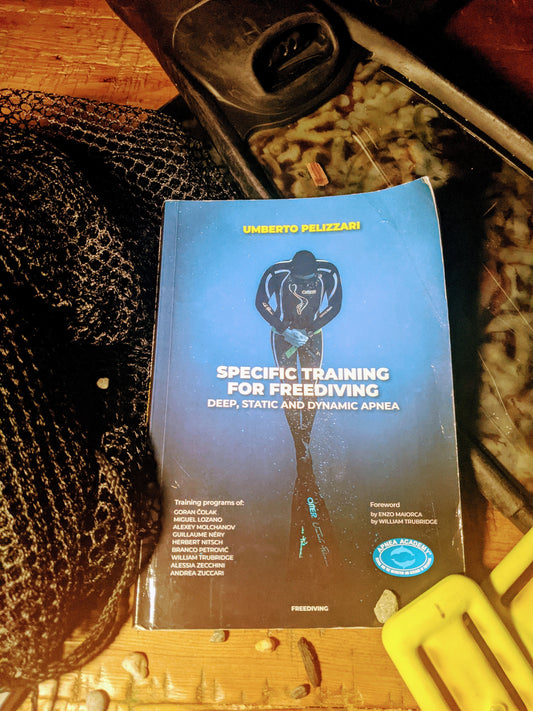 Freediving training manual by Umberto Pelizzari sitting on desk with fins, weight, and net